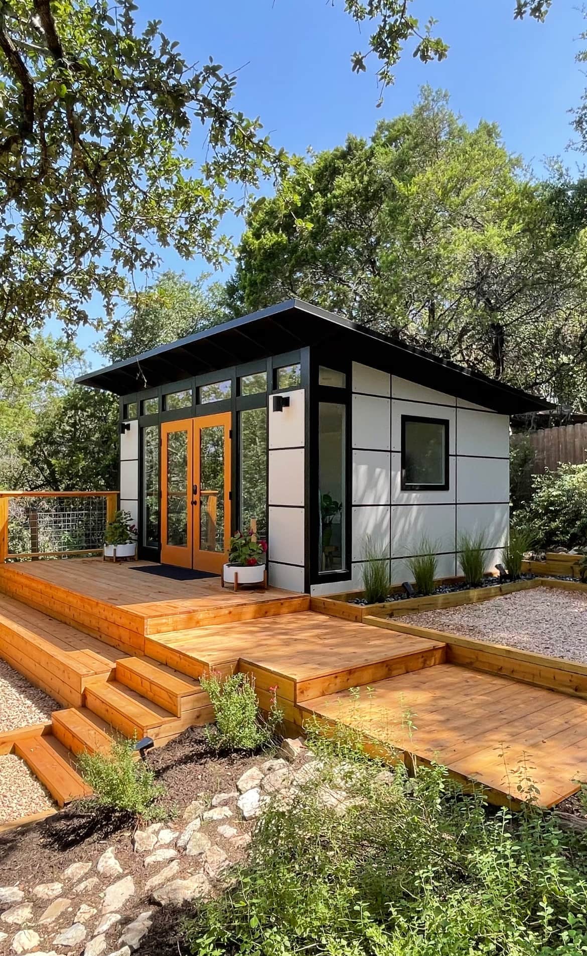 Studio Shed signature series unit with light block siding and orange french doors set on a custom deck with landscaping